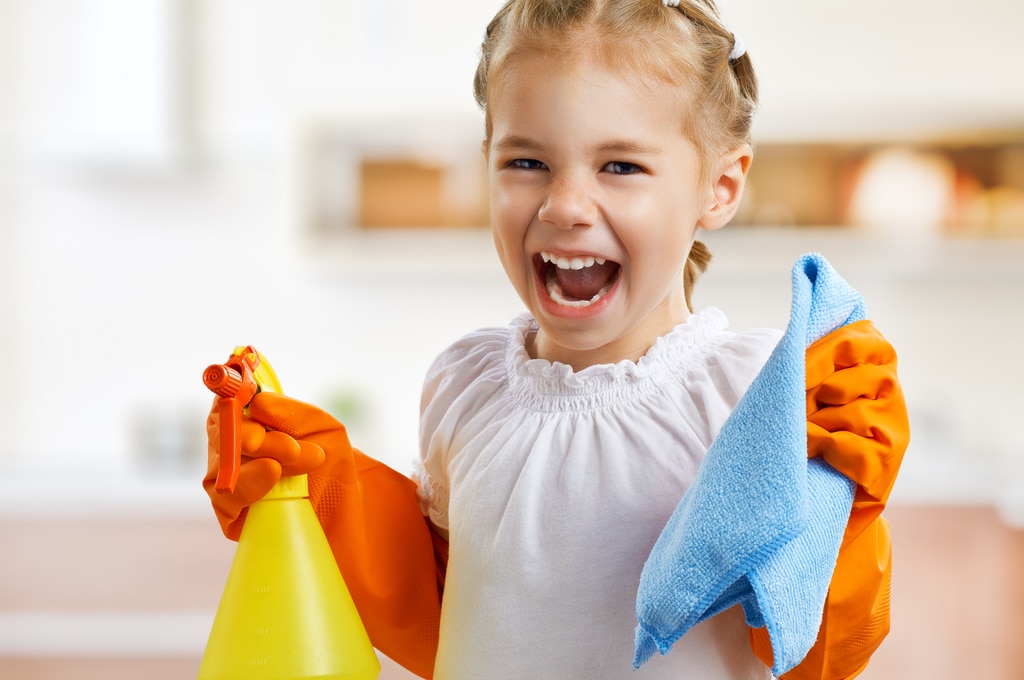happy little girl getting ready to practice spring cleaning tips with a blue towel in one hand and spray bottle in the other