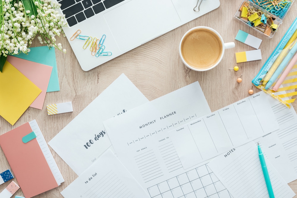 desktop photo with colorful flowers, laptop, and planners to plan for spring cleaning