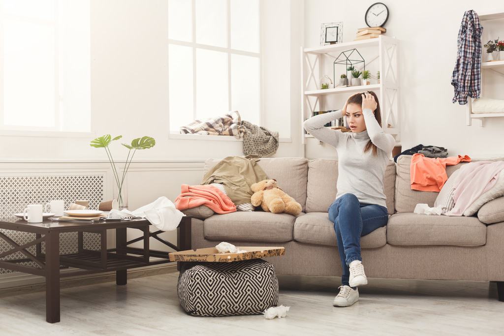 where to start decluttering?  woman sitting on couch stressed out by everyday messes that have been left out all over her living room